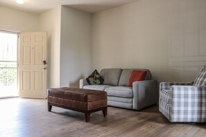 Una sala de estar con un sofá gris, un sillón escocés y un reposapiés marrón.