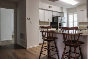 Una cocina con armarios blancos, un refrigerador de acero inoxidable y dos taburetes de madera.