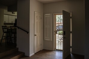 A hallway with a wooden staircase, a dining area with chairs, and a door leading outside.