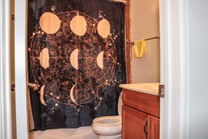 A bathroom with a black curtain featuring celestial designs, a white toilet, and wooden cabinets.