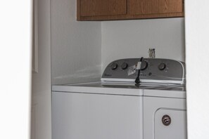 A front view of a white Whirlpool washer with a control panel, a wooden cabinet above, and a door with an 'AMERICA' logo.