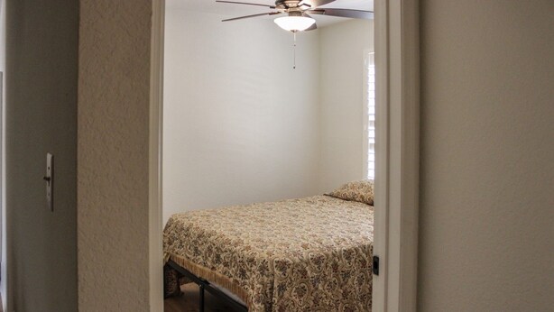 Quarto com uma cama, ventilador de teto e uma porta.