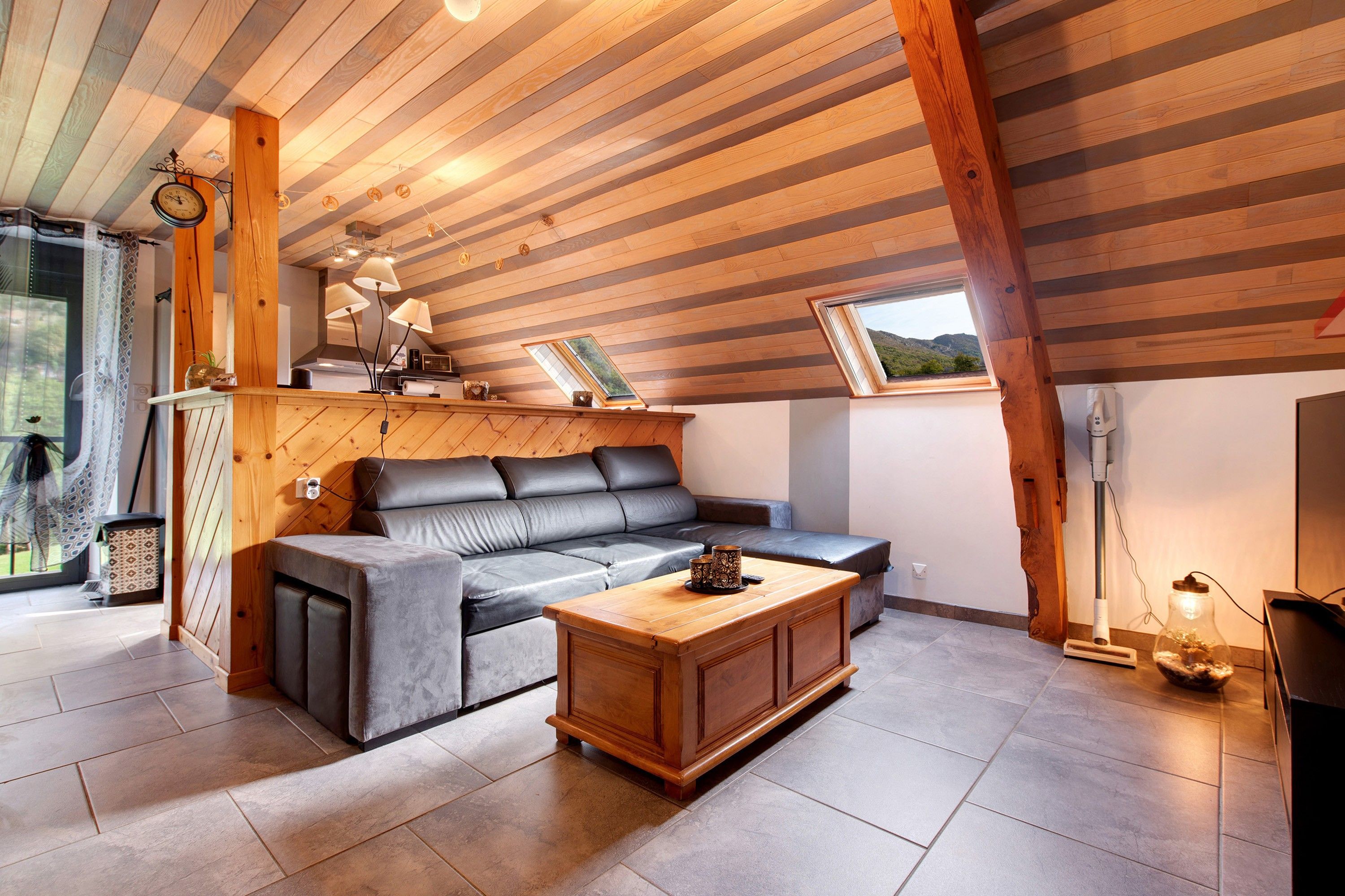 A modern living room with a wooden ceiling, a leather sofa, a wooden coffee table, and a view of the outdoors.