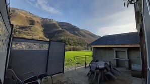 Eine Terrasse mit Sitzgelegenheiten, Blick auf ein grünes Feld und ein Berg im Hintergrund.