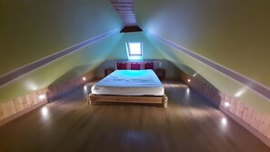 Una stanza con travi a vista, un letto, una finestra e una piccola finestra sul tetto.