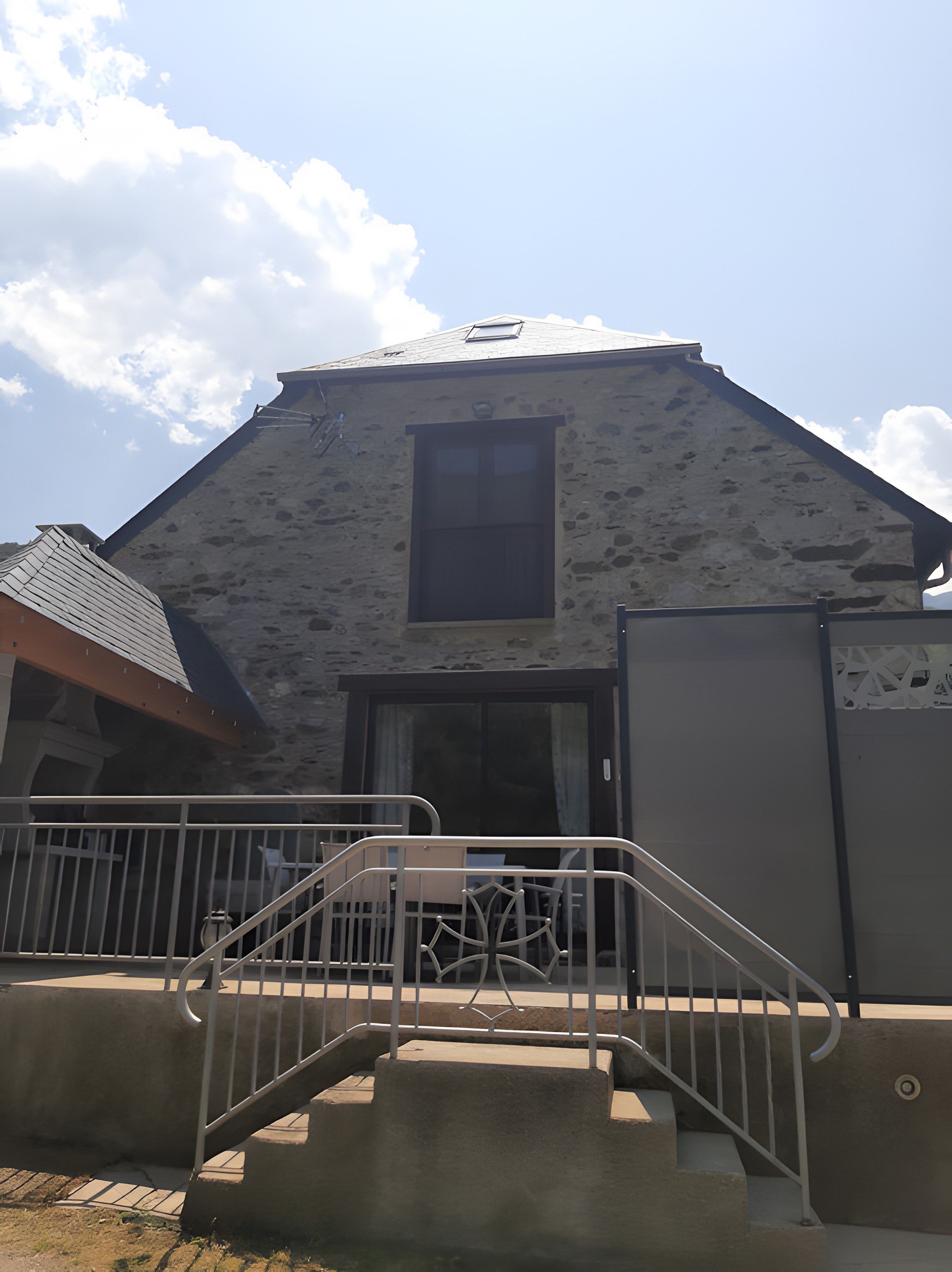 Un bâtiment doté d’une façade en pierre, d’une fenêtre centrale et d’un escalier menant à un balcon.