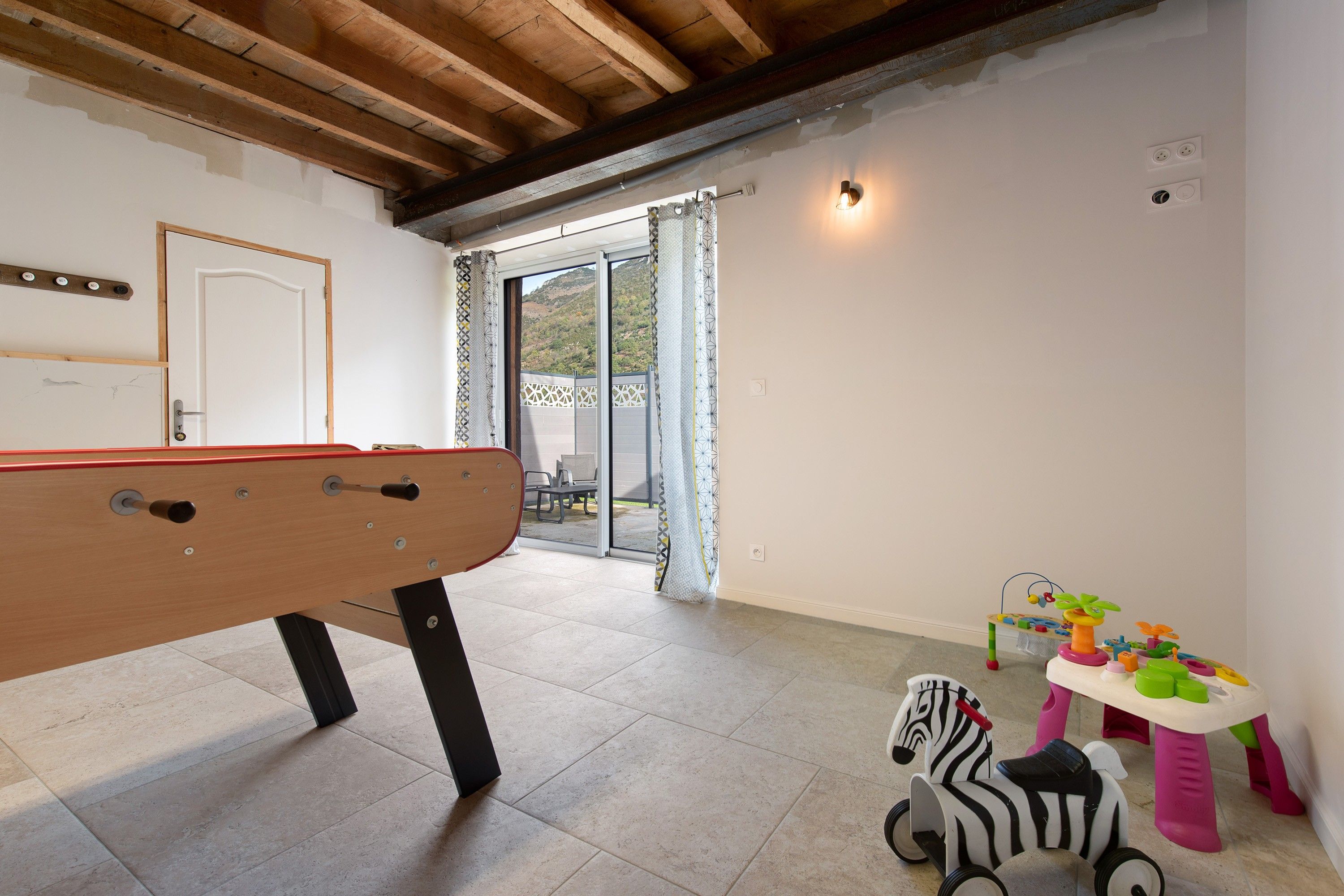 Habitación con mesa de billar, puerta corrediza de vidrio que da a un espacio exterior y juguetes infantiles.