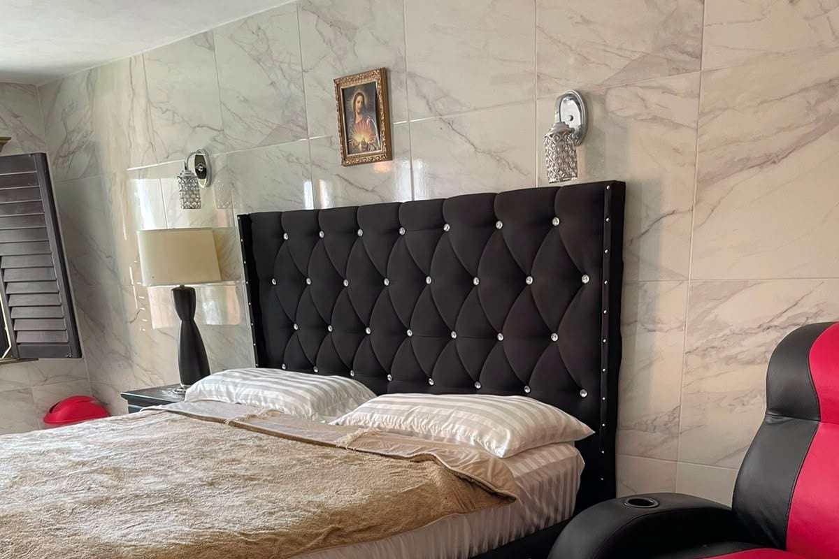 Una cama con cabecera acolchada, una silla negra y roja, y un cuadro en la pared.