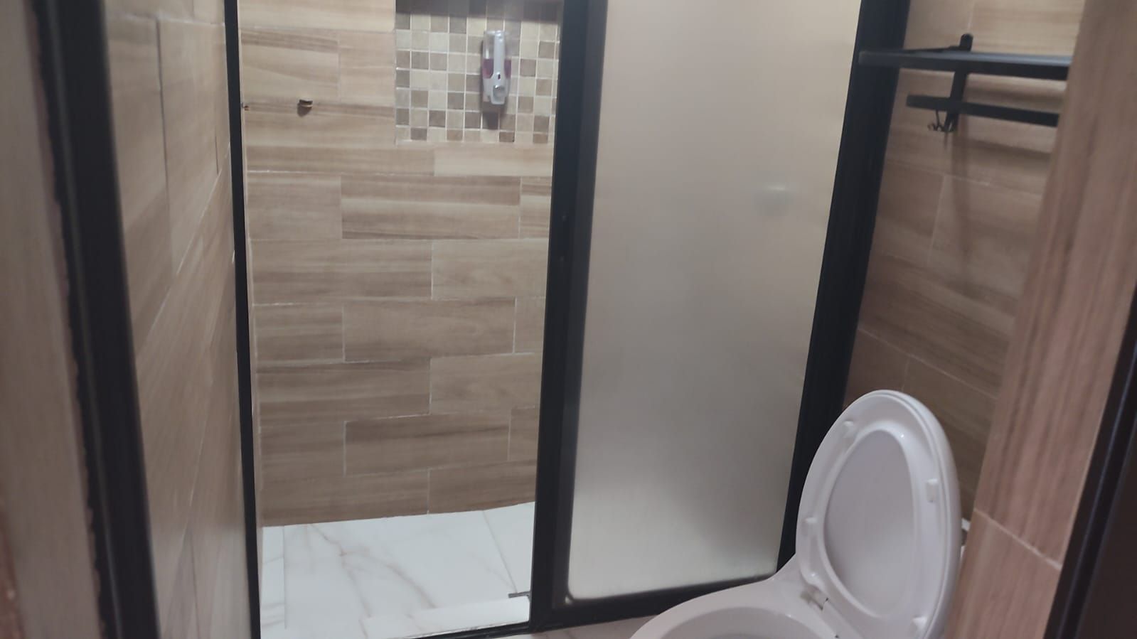 Un baño con inodoro, zona de ducha y pared de azulejos.