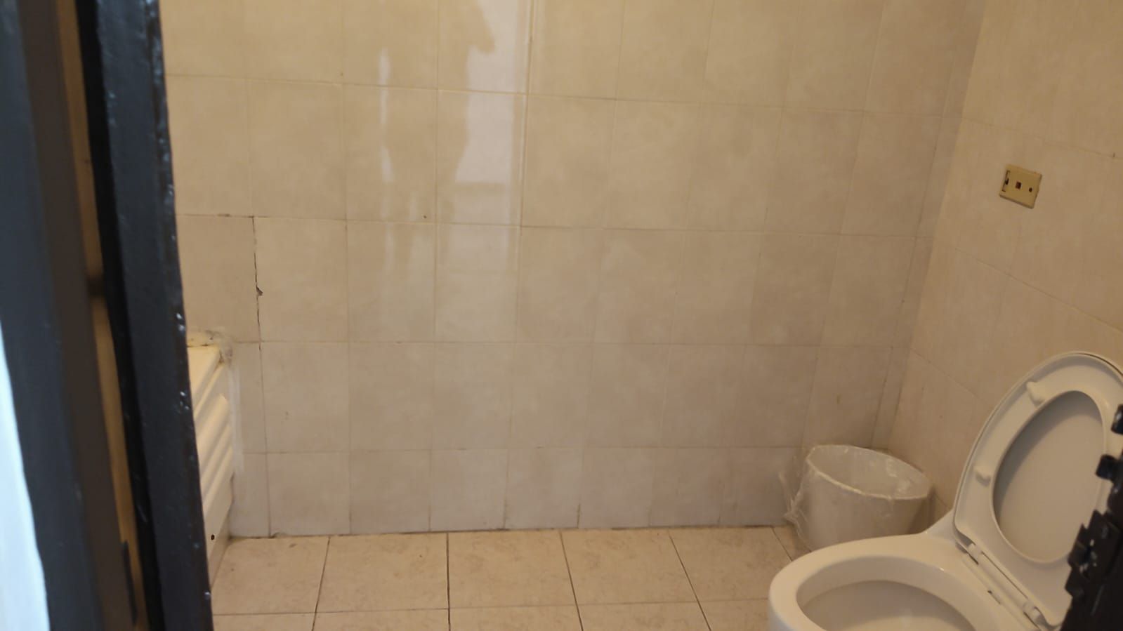 Un baño con inodoro, un pequeño bote de basura y una pared con azulejos.