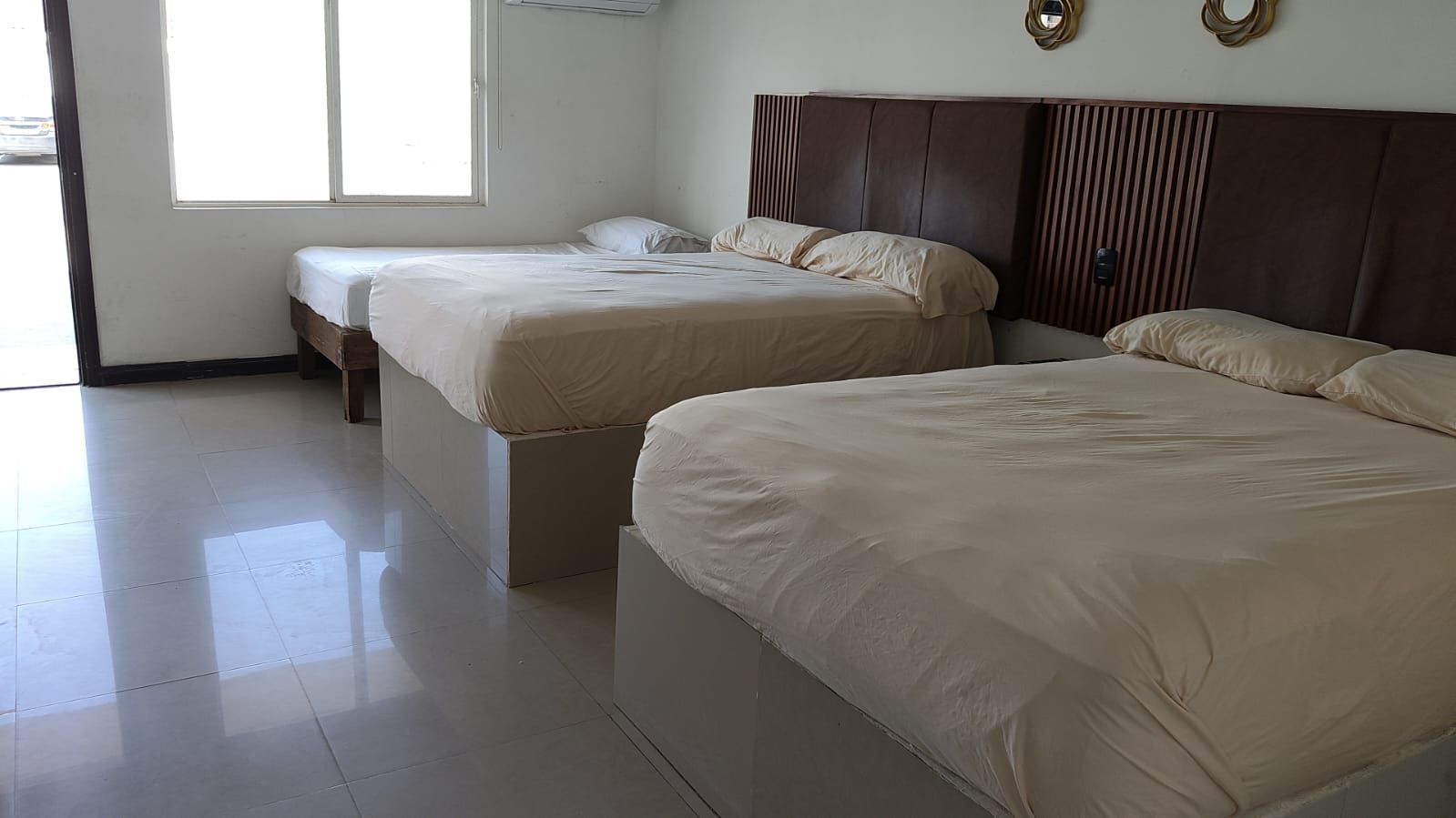 A hotel room with two beds, a bench, and a large window.