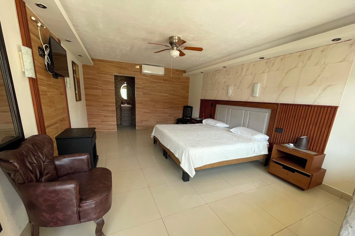 Un dormitorio con cama, una silla, un televisor y un ventilador de techo.