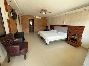 Un dormitorio con cama, una silla, un televisor y un ventilador de techo.