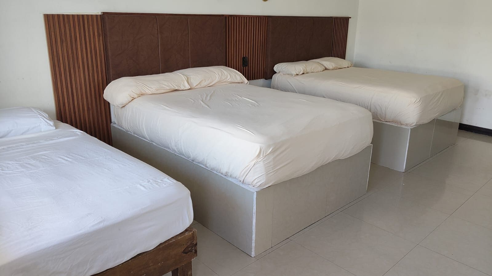A room with three beds arranged in a row, each with a wooden headboard and white bedding.