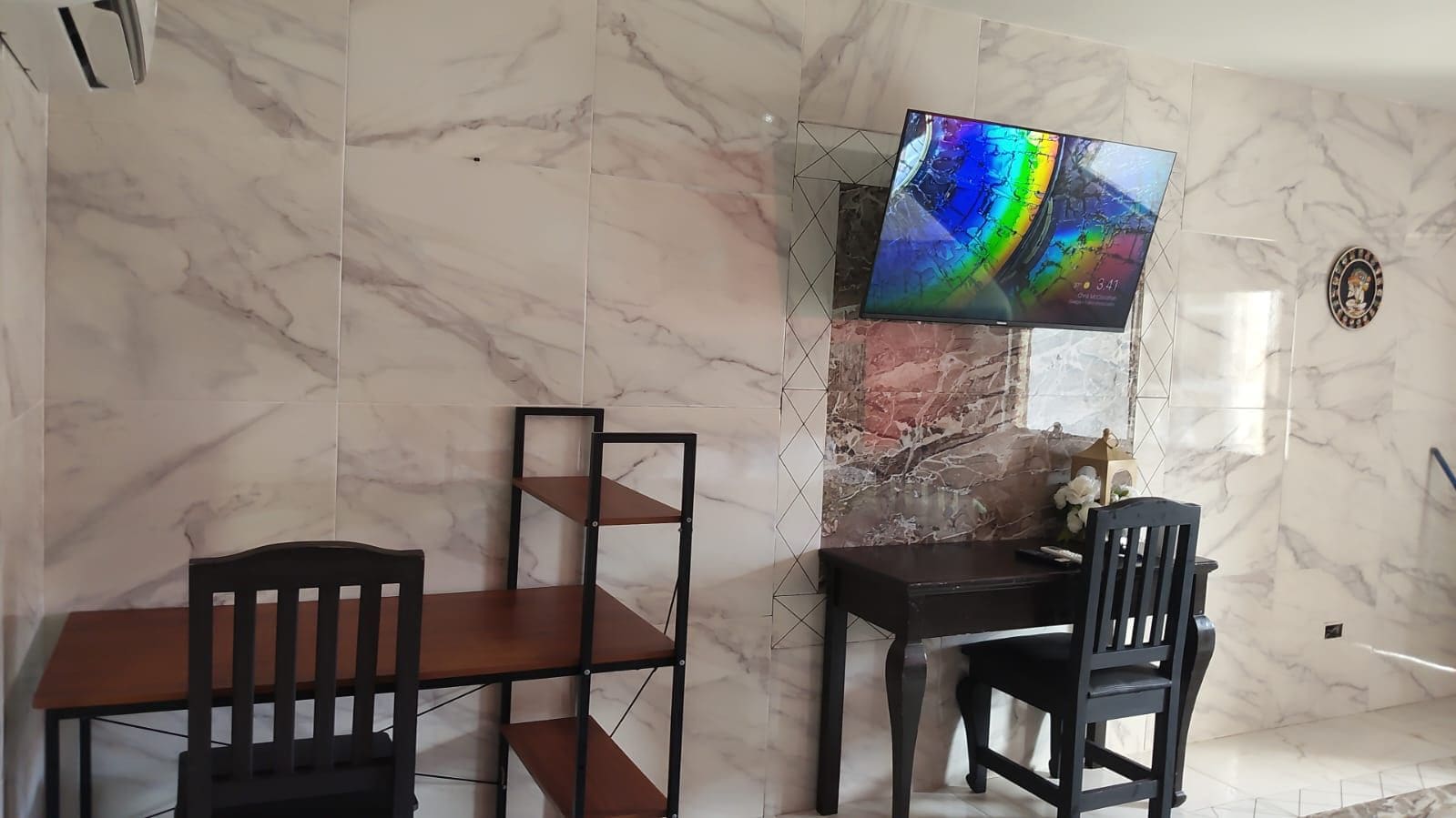 Una habitación con pared de mármol, un televisor montado en ella, una mesa de madera y dos sillas.