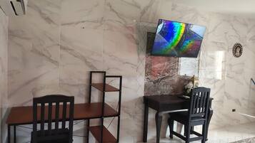 Una habitación con pared de mármol, un televisor montado en ella, una mesa de madera y dos sillas.
