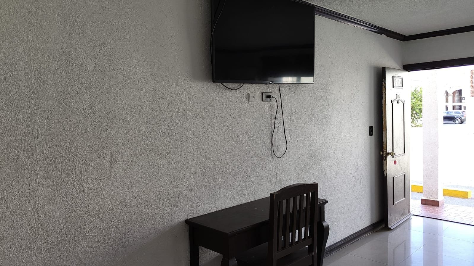 Ein Zimmer mit Fernseher, der an der Wand befestigt ist, einem Holztisch und einem Stuhl.