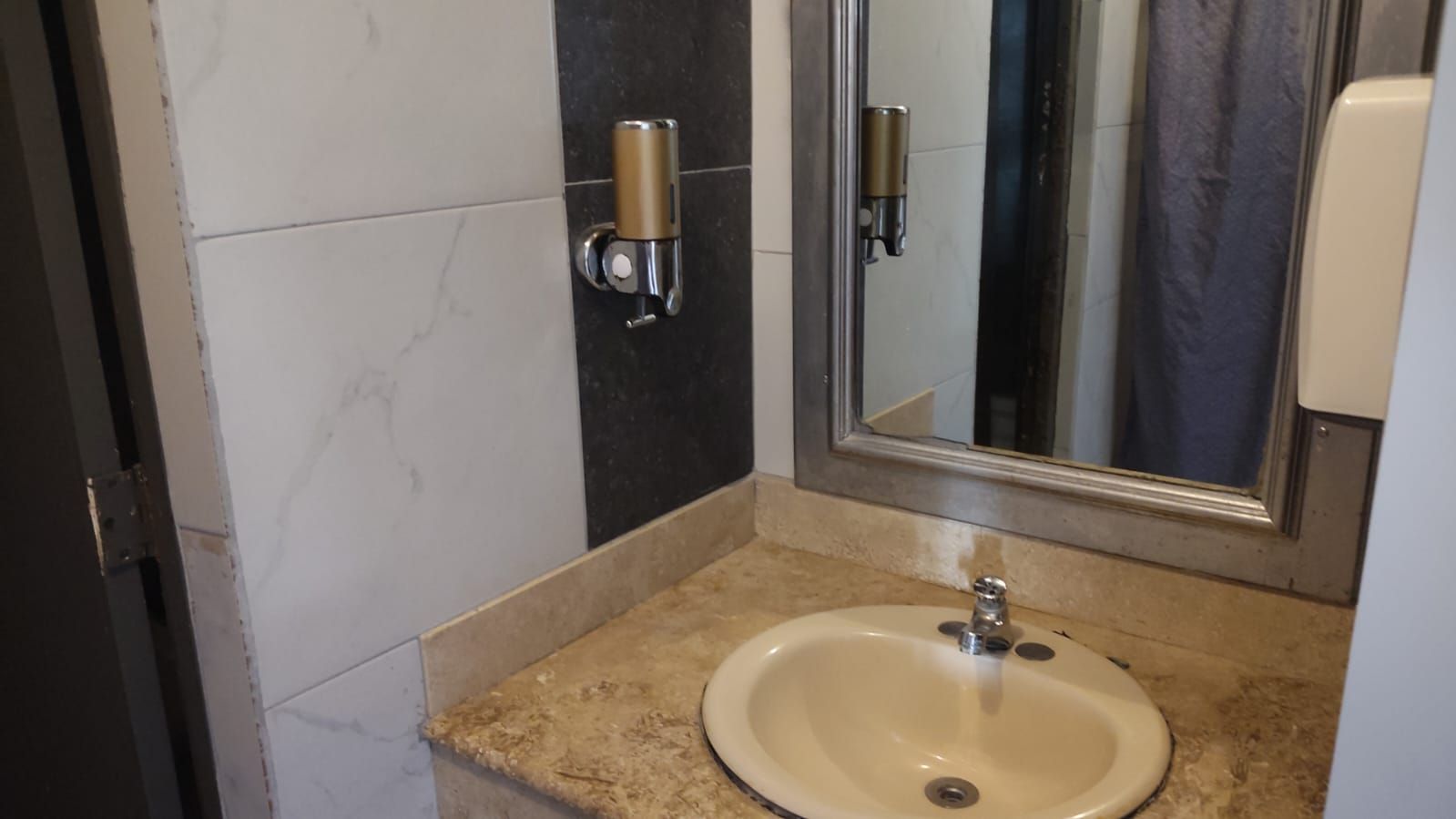 A bathroom with a sink, mirror, and towel dispenser.