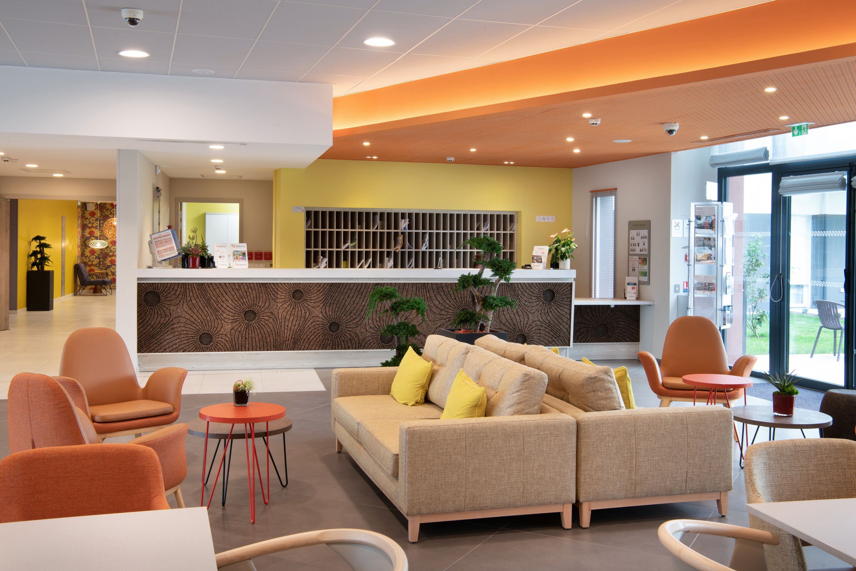 A modern lobby with a reception desk, seating area, and a large window.