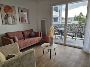 A modern living room with a sofa, a round table, and a view of the balcony.