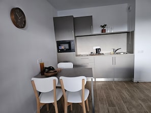 A modern kitchen with a microwave, sink, and cabinets. There is a dining table with chairs and a clock on the wall.