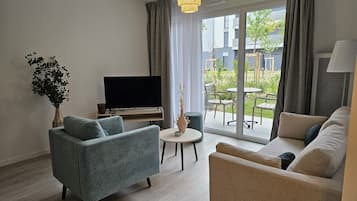 A modern living room with a flat-screen TV, two sofas, a small round table, and a potted plant.
