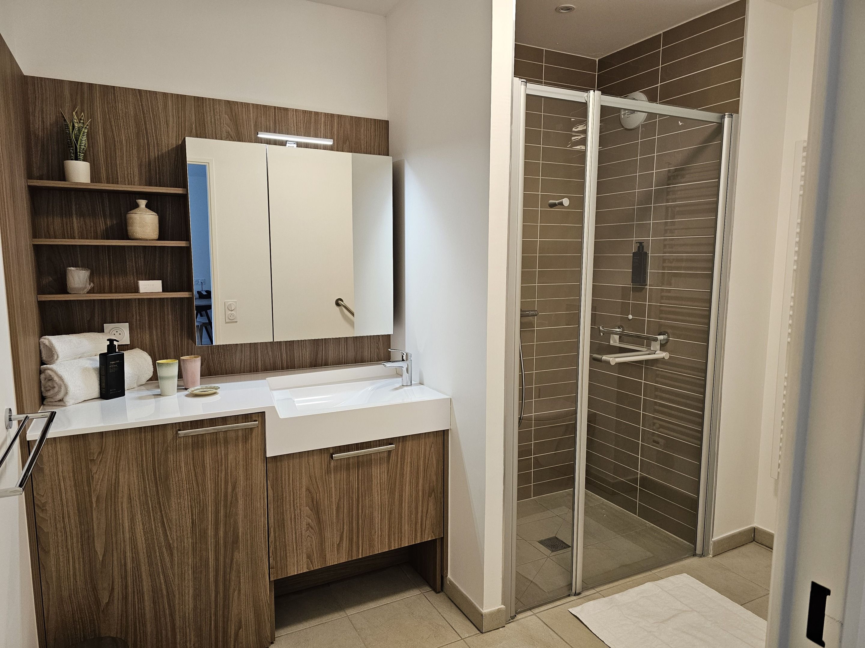 Een moderne badkamer met een houten wastafelmeubel, een grote spiegel, een douchecabine van glas en een witte wasbak.
