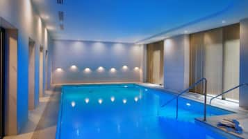 Una piscina interior con vista despejada al área de la piscina, incluyendo el borde, las escaleras de acceso y un conjunto de escalones que bajan a la piscina.