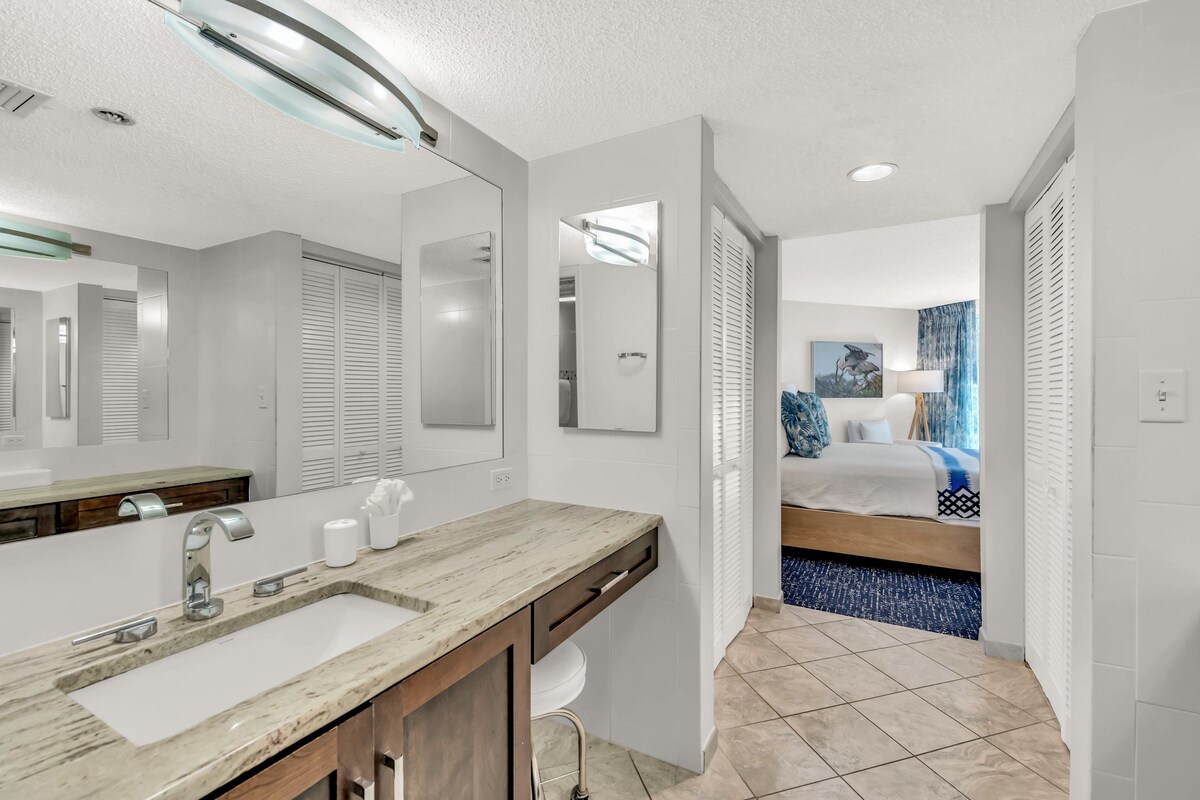 A modern bathroom with a marble sink, a mirror, and a shower area.