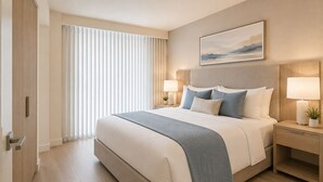 A hotel room with a large bed, bedside lamps, a nightstand, a window with blinds, and a painting on the wall. - Downtown Top Suites - S Avenue  (Toronto)