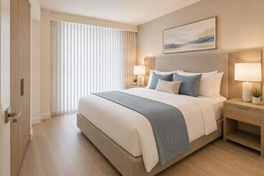 Habitación de hotel con una cama grande, lámparas de noche, mesita de noche, ventana con persianas y un cuadro en la pared.