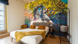 Ein Schlafzimmer mit einem großen Bett, einem farbenfrohen Wandgemälde und einem Fenster mit Blick.
