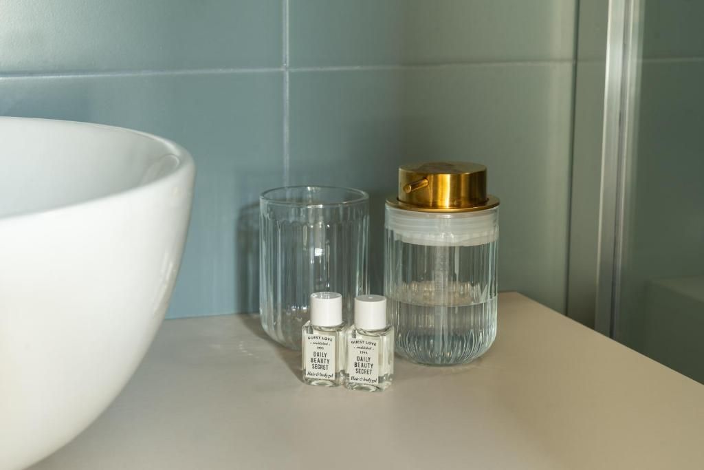 A bathroom counter with a large white basin, a clear glass, and two small bottles labeled 'Guest Love Daily Beauty Secret.'