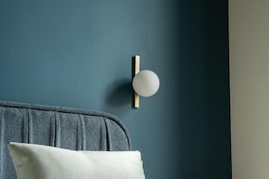 A room with a grey headboard, a white pillow, and a wall-mounted light fixture.