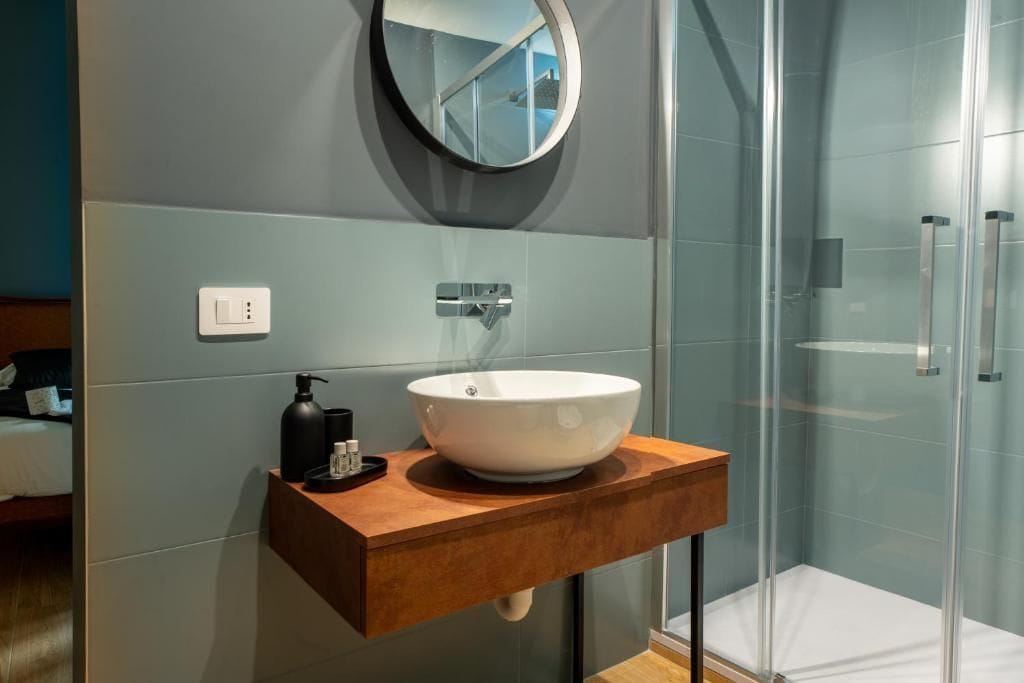Un baño con un lavamanos blanco tipo recipiente, un espejo redondo y una cabina de ducha de vidrio.