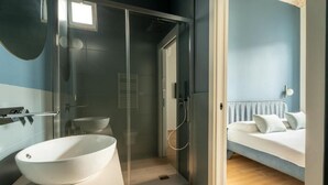 A modern bathroom with a glass-enclosed shower, a white sink, and a bed with white bedding in the adjacent room. - B&B YUTORI 75 (Altamura)