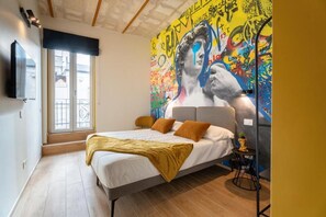 Une chambre à coucher avec un lit, une fenêtre, une fresque murale et un téléviseur fixé au mur.