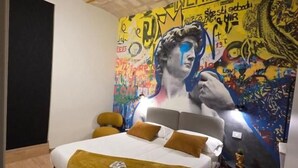 Ein Schlafzimmer mit einem Bett, einem Kopfteil, einem Nachttisch und einer Wand mit einem farbenfrohen Wandgemälde.