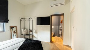 Un dormitorio con cama, televisor montado en la pared, armario y baño visible a través de una puerta abierta.