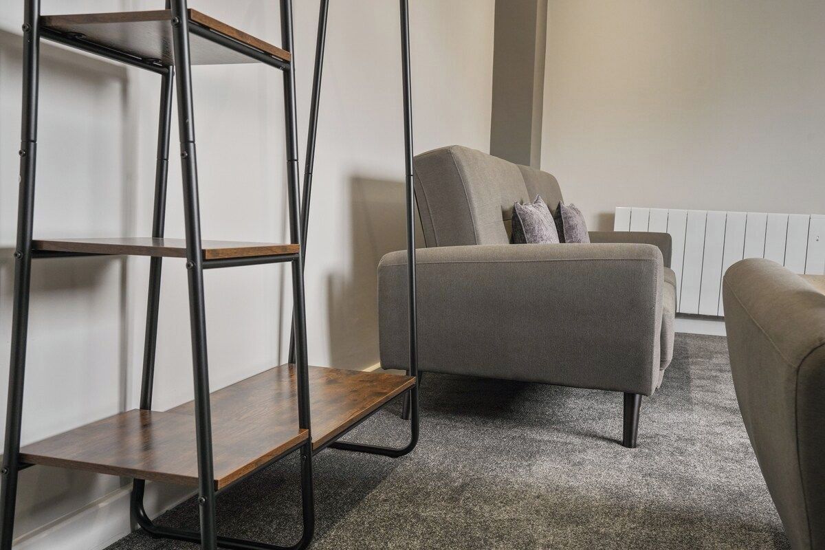 A room with a grey sofa, a wooden shelf unit, and a radiator.