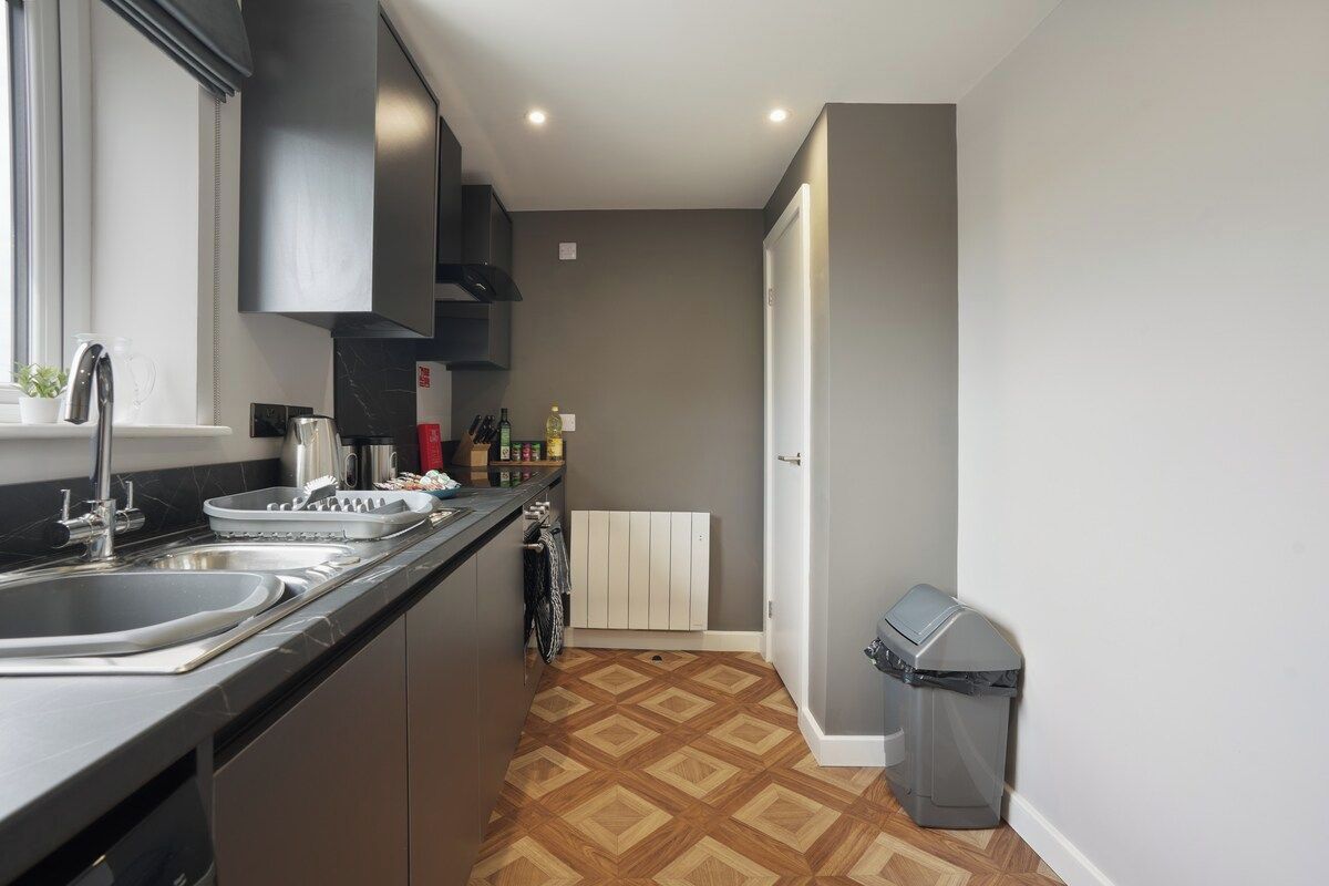 A modern kitchen with a black countertop, stainless steel sink, and a built-in oven.