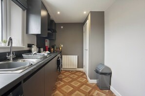 A modern kitchen with a black countertop, stainless steel sink, and a built-in oven. - The Olive Tree | Deluxe 1-Bed Apartment (Kingston upon Hull)