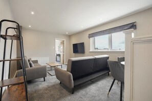 A modern living room with a sofa, chairs, a TV, and a window. - The Olive Tree | Deluxe 1-Bed Apartment (Kingston upon Hull)