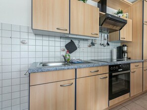 A modern kitchen with wooden cabinets, a stainless steel sink, and a built-in oven. - Holiday Apartment 2 in Haus Hever (St. Peter-Ording)