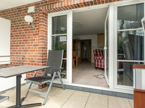 A patio area with a table and chairs, a brick wall, and a sliding glass door leading to an interior space. - Holiday Apartment 2 in Haus Hever (St. Peter-Ording)