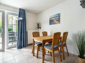 A dining area with a wooden table and chairs, a potted plant, a painting, and a view through a glass door. - Holiday Apartment 2 in Haus Hever (St. Peter-Ording)