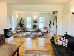 Ein geräumiges Wohnzimmer mit Holzboden, einer schwarzen Ledersofa, einem weißen Sessel, einem Couchtisch und einem Bücherregal.