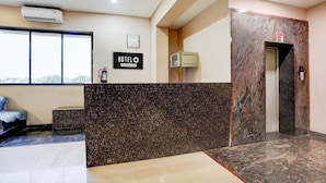 A hotel reception area with a marble counter, a sign reading 'HOTELO,' an elevator, and a window with a view. - Hotel O Rani Durgawati Crossway (Nagpur)