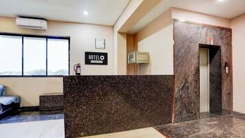 A hotel reception area with a marble counter, a sign reading 'HOTELO,' an elevator, and a window with a view.