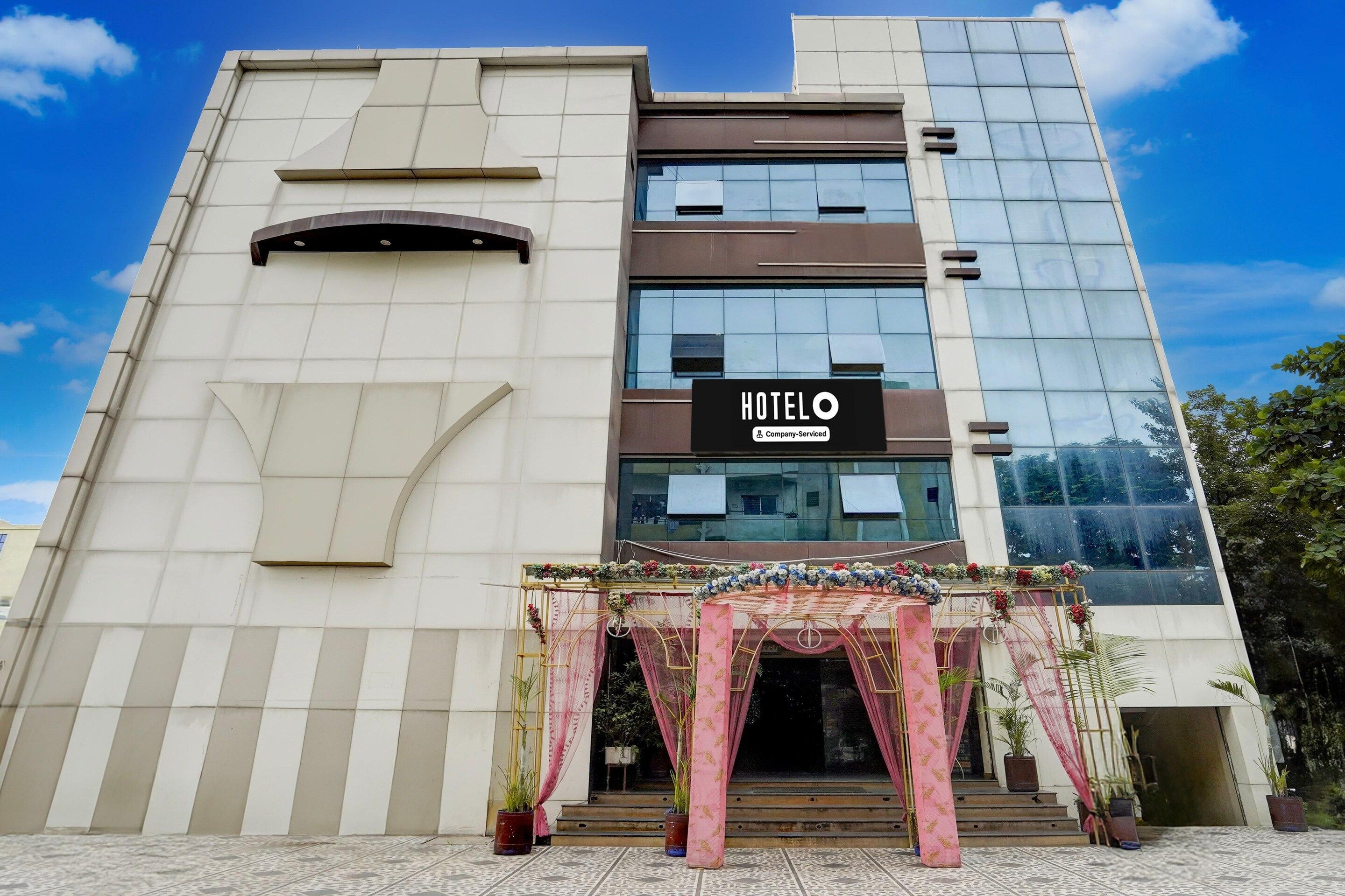 A modern hotel building with a prominent 'HOTEL' sign, a glass facade, and a decorative entrance with potted plants.